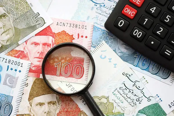 Pakistan banknotları ve büyüteçle hesap makinesi. Mevcut Pakistan para faturaları ve loupe ile calc büyük miktarda masada yatıyor. Pakistan 'da vergi ve para sayımı kavramı