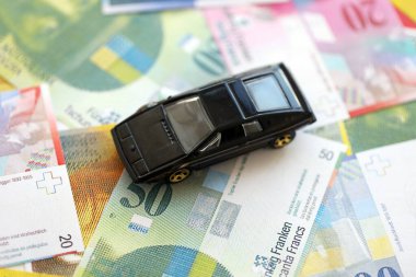 İsviçre frangı banknotları ve oyuncak araba. Mevcut frank, faturalar ve siyah araba büyük miktarda masada yatıyor. İsviçre 'de araba sahibi olma kavramı