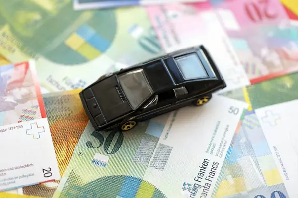 İsviçre frangı banknotları ve oyuncak araba. Mevcut frank, faturalar ve siyah araba büyük miktarda masada yatıyor. İsviçre 'de araba sahibi olma kavramı