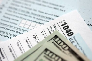 Yüz dolarlık banknotlar ve 1040 bireysel gelir vergisi iade formu yakın çekim. Çok az Amerikan doları ve Birleşik Devletler vergisi yok. ABD 'de vergi ödeme ve muhasebe kavramı