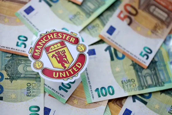 KYIV, UKRAINE - 23 Şubat 2025 Manchester United FC futbol kulübü rozeti büyük miktarda EURO para banknotlarının üzerinde yatıyor