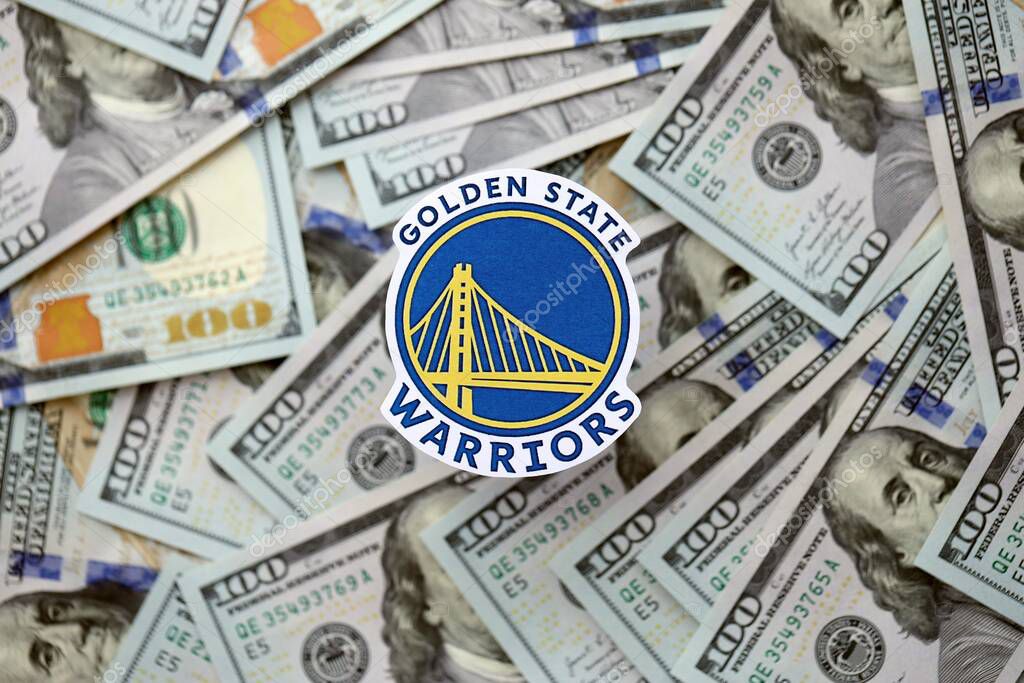 KYIV, UKRAINE - FEBRUARY 23, 2025 Golden State Warriors basketball team badge lies on big amount of hundred US dollar bills close up