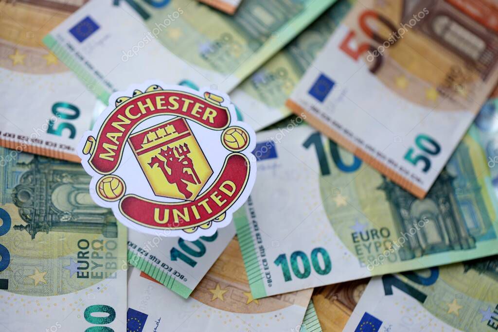 KYIV, UKRAINE - FEBRUARY 23, 2025 Manchester United FC football club badge lies on big amount of hundred EURO money bills