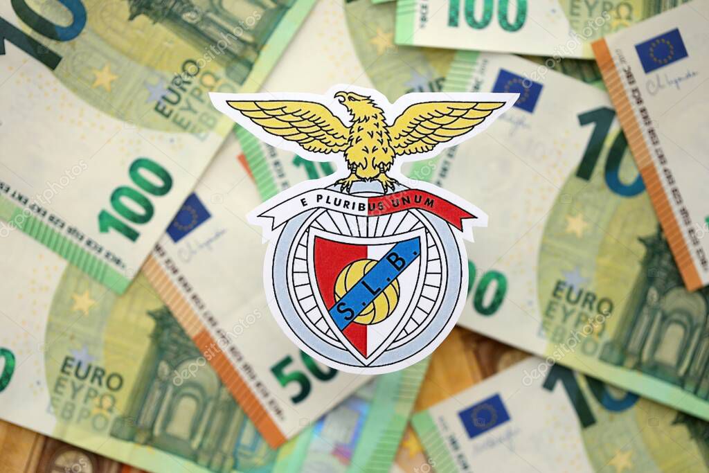 KYIV, UKRAINE - FEBRUARY 23, 2025 Sport Lisboa e Benfica football club badge lies on big amount of hundred EURO money bills