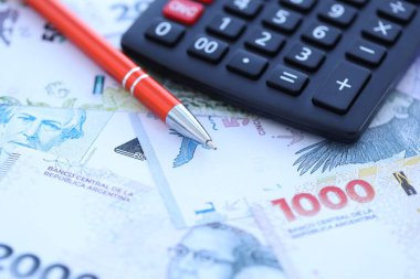 Arjantin Pezosu 'nun büyük miktarlarda para banknotları kalem ve hesap makinesiyle masanın üzerinde duruyor. Maliye ve vergi ödeme kavramı
