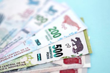 Arjantin Pezosu 'nun büyük miktarlarda para banknotları yakın planda, deniz mavisi renkli masada yatıyor. Finans ve bankacılık kavramı