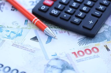 Arjantin Pezosu 'nun büyük miktarlarda para banknotları kalem ve hesap makinesiyle masanın üzerinde duruyor. Maliye ve vergi ödeme kavramı