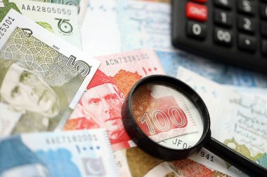 Pakistan banknotları ve büyüteçle hesap makinesi. Mevcut Pakistan para faturaları ve loupe ile calc büyük miktarda masada yatıyor. Pakistan 'da vergi ve para sayımı kavramı