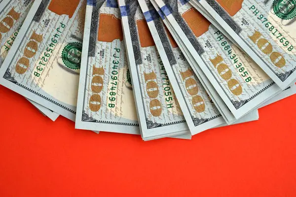 Kırmızı arka planda büyük miktarda yüz dolarlık banknot var. ABD 'de vergilendirme ve para yapma kavramı