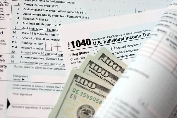 Yüz dolarlık banknotlar ve 1040 bireysel gelir vergisi iade formu yakın çekim. Çok az Amerikan doları ve Birleşik Devletler vergisi yok. ABD 'de vergi ödeme ve muhasebe kavramı
