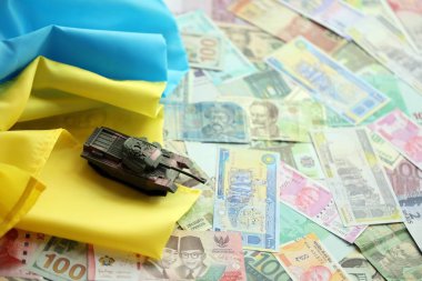 Ukrayna bayrağında farklı para birimlerinde oyuncak tankı. Ukrayna 'daki savaş finansmanı ve askeri destek fiyatlarının geçmişi