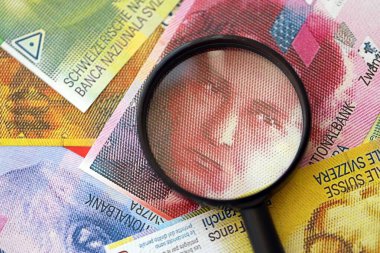 İsviçre frangı banknotları ve büyüteç. İçinde loupe olan şu anki para banknotları büyük miktarda masada yatıyor. İsviçre 'de mali izleme ve vergilendirme kavramı