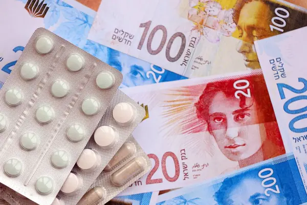 Israel New Shekels banknotları ve ilaç hapları. Mevcut İsrail para ve uyuşturucu faturaları büyük miktarda masada yatıyor. İsrail 'de ilaç ve eczane kavramı