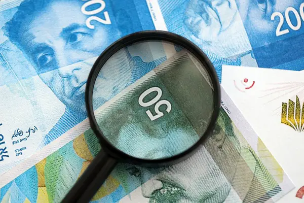 Israel New Shekels banknotları ve büyüteç. Şu anki İsrail 'in yüksek meblağlı faturaları masanın üzerinde yatıyor. İsrail 'de mali izleme ve vergilendirme kavramı