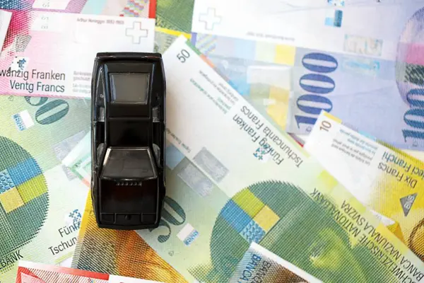 İsviçre frangı banknotları ve oyuncak araba. Mevcut frank, faturalar ve siyah araba büyük miktarda masada yatıyor. İsviçre 'de araba sahibi olma kavramı