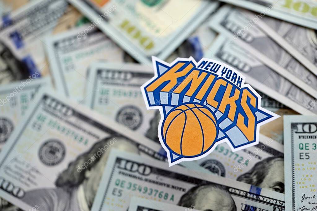 KYIV, UKRAINE - FEBRUARY 23, 2025 New York Knicks basketball team badge lies on big amount of hundred US dollar bills close up