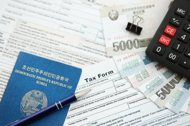 Kuzey Kore büyük miktarlarda para kazandı. Masada kalem, hesap makinesi, pasaport ve vergi formları var. Vergi ödeme ve muhasebe kavramı