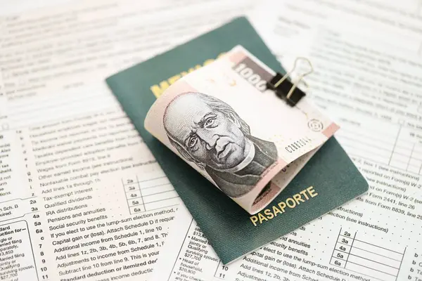 Meksika Pezosu 'nun büyük meblağlı para faturaları pasaport ve vergi formlarıyla birlikte masanın üzerinde duruyor. Maliye ve vergi ödeme kavramı