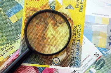 İsviçre frangı banknotları ve büyüteç. İçinde loupe olan şu anki para banknotları büyük miktarda masada yatıyor. İsviçre 'de mali izleme ve vergilendirme kavramı
