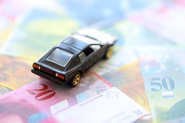 İsviçre frangı banknotları ve oyuncak araba. Mevcut frank, faturalar ve siyah araba büyük miktarda masada yatıyor. İsviçre 'de araba sahibi olma kavramı