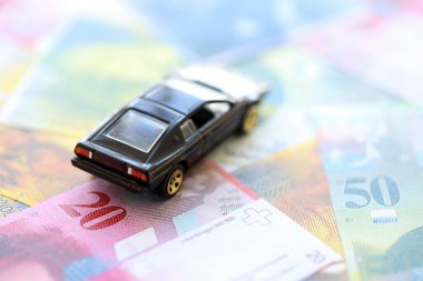 İsviçre frangı banknotları ve oyuncak araba. Mevcut frank, faturalar ve siyah araba büyük miktarda masada yatıyor. İsviçre 'de araba sahibi olma kavramı