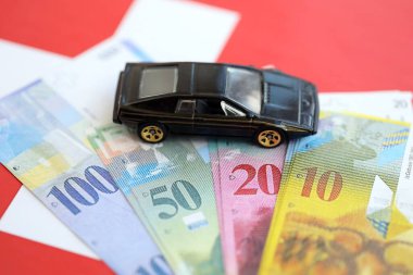 İsviçre frangı banknotları ve bayrak üstünde oyuncak araba. Mevcut frank, faturalar ve siyah araba bayrağın üzerinde duruyor. İsviçre 'de araba sahibi olma kavramı