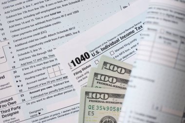 Yüz dolarlık banknotlar ve 1040 bireysel gelir vergisi iade formu yakın çekim. Çok az Amerikan doları ve Birleşik Devletler vergisi yok. ABD 'de vergi ödeme ve muhasebe kavramı