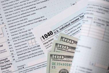 Yüz dolarlık banknotlar ve 1040 bireysel gelir vergisi iade formu yakın çekim. Çok az Amerikan doları ve Birleşik Devletler vergisi yok. ABD 'de vergi ödeme ve muhasebe kavramı