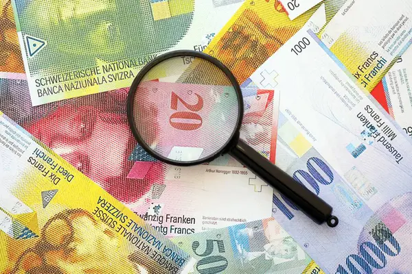 İsviçre frangı banknotları ve büyüteç. İçinde loupe olan şu anki para banknotları büyük miktarda masada yatıyor. İsviçre 'de mali izleme ve vergilendirme kavramı