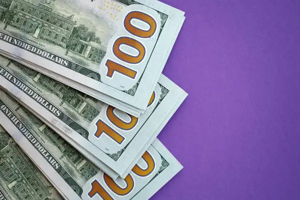 Mor arka planda büyük miktarda yüz dolarlık banknotlar. ABD 'de vergilendirme ve para yapma kavramı