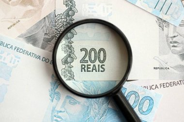 Brezilya reais banknotları ve büyüteç. Mevcut Brezilya gerçek para faturaları ve loupe büyük miktarda masada yatıyor. Brezilya 'da mali izleme ve vergilendirme kavramı