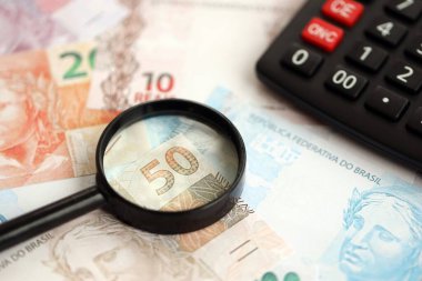 Brezilya reais banknotları ve büyüteçli hesap makinesi. Mevcut Brezilya gerçek para faturaları ve loupe ile calc büyük miktarda masada yatıyor. Brezilya 'da vergilendirme ve para konsepti
