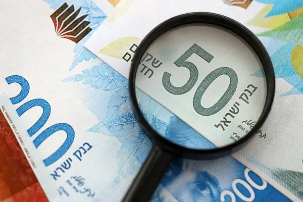 Israel New Shekels banknotları ve büyüteç. Şu anki İsrail 'in yüksek meblağlı faturaları masanın üzerinde yatıyor. İsrail 'de mali izleme ve vergilendirme kavramı