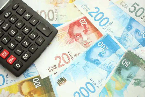 Israel New Shekels banknotları ve hesap makinesi. Mevcut İsrail para faturaları ve kalibreleri büyük miktarda masada yatıyor. İsrail 'de vergilendirme ve para kavramı