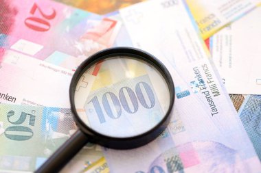 İsviçre frangı banknotları ve büyüteç. İçinde loupe olan şu anki para banknotları büyük miktarda masada yatıyor. İsviçre 'de mali izleme ve vergilendirme kavramı