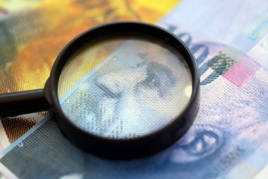 İsviçre frangı banknotları ve büyüteç. İçinde loupe olan şu anki para banknotları büyük miktarda masada yatıyor. İsviçre 'de mali izleme ve vergilendirme kavramı