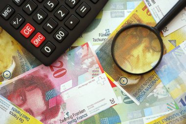 İsviçre frangı banknotları ve büyüteçli hesap makinesi. Mevcut para faturaları ve loupe ile calc büyük miktarda masada yatıyor. İsviçre 'de vergilendirme ve iş kavramı