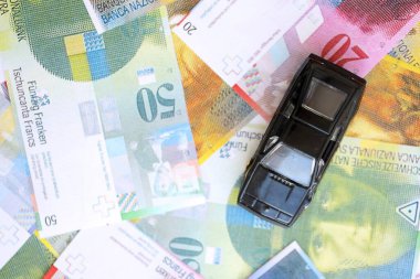 İsviçre frangı banknotları ve oyuncak araba. Mevcut frank, faturalar ve siyah araba büyük miktarda masada yatıyor. İsviçre 'de araba sahibi olma kavramı