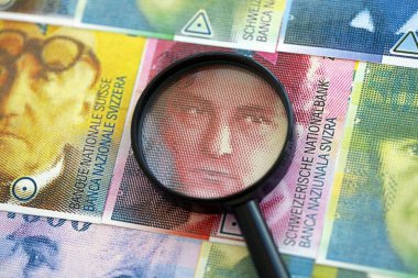 İsviçre frangı banknotları ve büyüteç. Loupe 'un para faturaları büyük miktarda masada duruyor. İsviçre 'de mali izleme ve vergilendirme kavramı