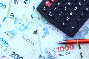 Arjantin Pezosu 'nun büyük miktarlarda para banknotları kalem ve hesap makinesiyle masanın üzerinde duruyor. Maliye ve vergi ödeme kavramı