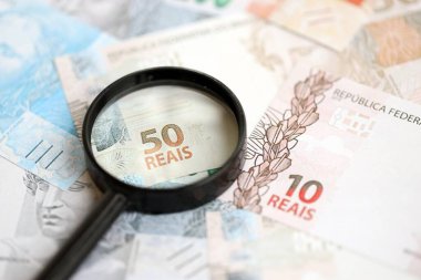 Brezilya reais banknotları ve büyüteç. Mevcut Brezilya gerçek para faturaları ve loupe büyük miktarda masada yatıyor. Brezilya 'da mali izleme ve vergilendirme kavramı