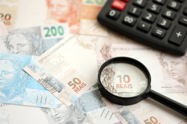 Brezilya reais banknotları ve büyüteçli hesap makinesi. Mevcut Brezilya gerçek para faturaları ve loupe ile calc büyük miktarda masada yatıyor. Brezilya 'da vergilendirme ve para konsepti