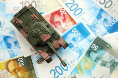 Israel New Shekels banknotları ve oyuncak tankı. İsrail 'in şu anki para ve tankı büyük miktarda masanın üzerinde duruyor. İsrail 'de ordu fonları ve silah satışları kavramı
