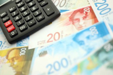 Israel New Shekels banknotları ve hesap makinesi. Mevcut İsrail para faturaları ve kalibreleri büyük miktarda masada yatıyor. İsrail 'de vergilendirme ve para kavramı