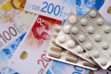 Israel New Shekels banknotları ve ilaç hapları. Mevcut İsrail para ve uyuşturucu faturaları büyük miktarda masada yatıyor. İsrail 'de ilaç ve eczane kavramı