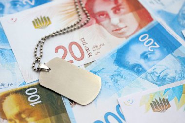 İsrail Yeni Şekelleri 'nin banknotları ve askeri simgesi. İsrail 'in mevcut para faturaları ve künyeleri büyük miktarda masada yatıyor. İsrail 'de askerlik kavramı