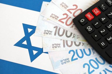 Israel New Shekels banknotları ve hesap makinesi bayrağın üzerinde. İsrail 'in mevcut para faturaları ve kalibreleri büyük oranda bayrakta yatıyor. İsrail 'de vergilendirme ve para kavramı