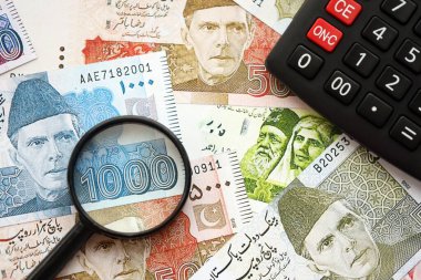 Pakistan banknotları ve büyüteçle hesap makinesi. Mevcut Pakistan para faturaları ve loupe ile calc büyük miktarda masada yatıyor. Pakistan 'da vergi ve para sayımı kavramı