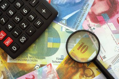 İsviçre frangı banknotları ve büyüteçli hesap makinesi. Mevcut para faturaları ve loupe ile calc büyük miktarda masada yatıyor. İsviçre 'de vergilendirme ve iş kavramı