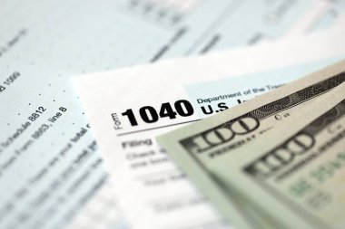 Yüz dolarlık banknotlar ve 1040 bireysel gelir vergisi iade formu yakın çekim. Çok az Amerikan doları ve Birleşik Devletler vergisi yok. ABD 'de vergi ödeme ve muhasebe kavramı